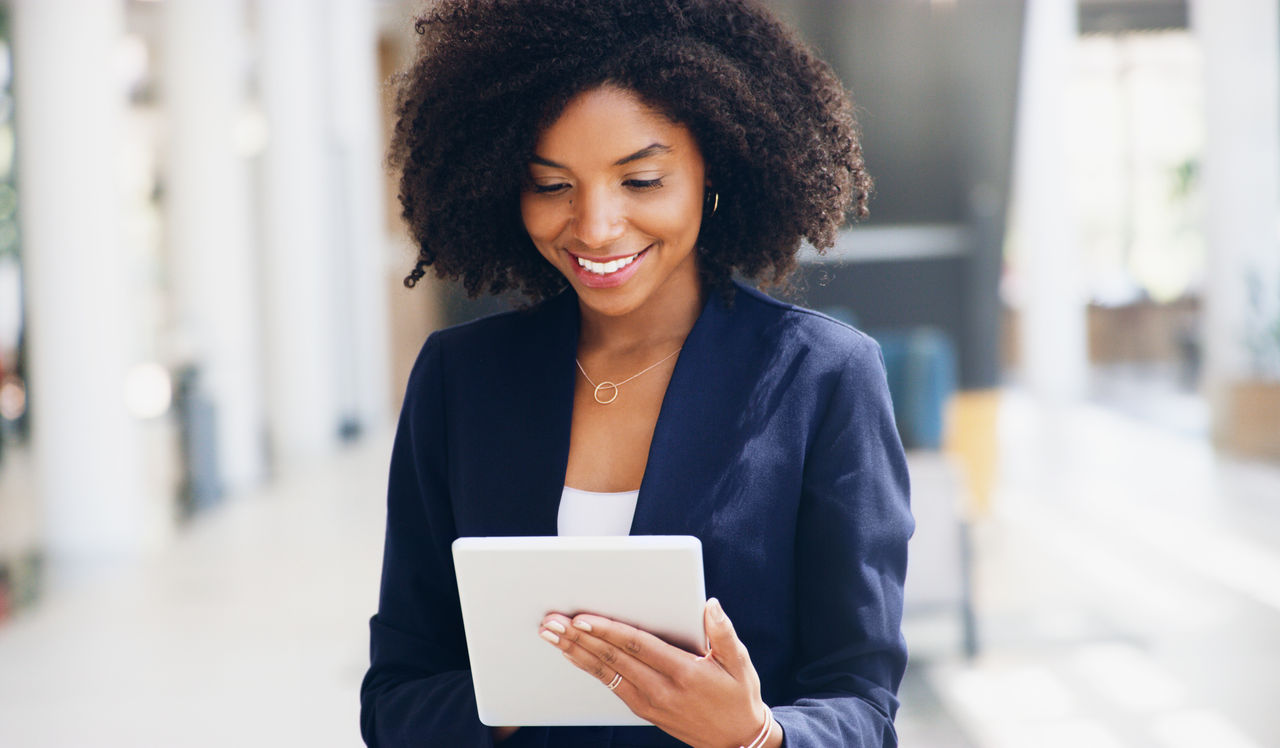 Cropped shot of an attractive young businesswoman standing alone and using a tablet while in the office during the day