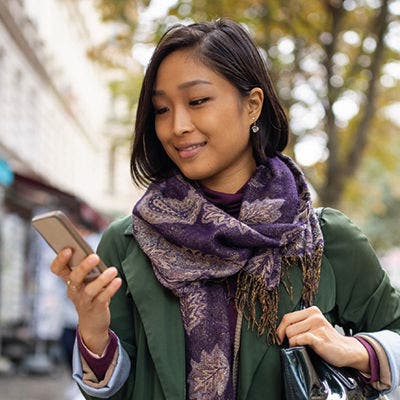 Person walking outdoors while looking at a mobile phone.